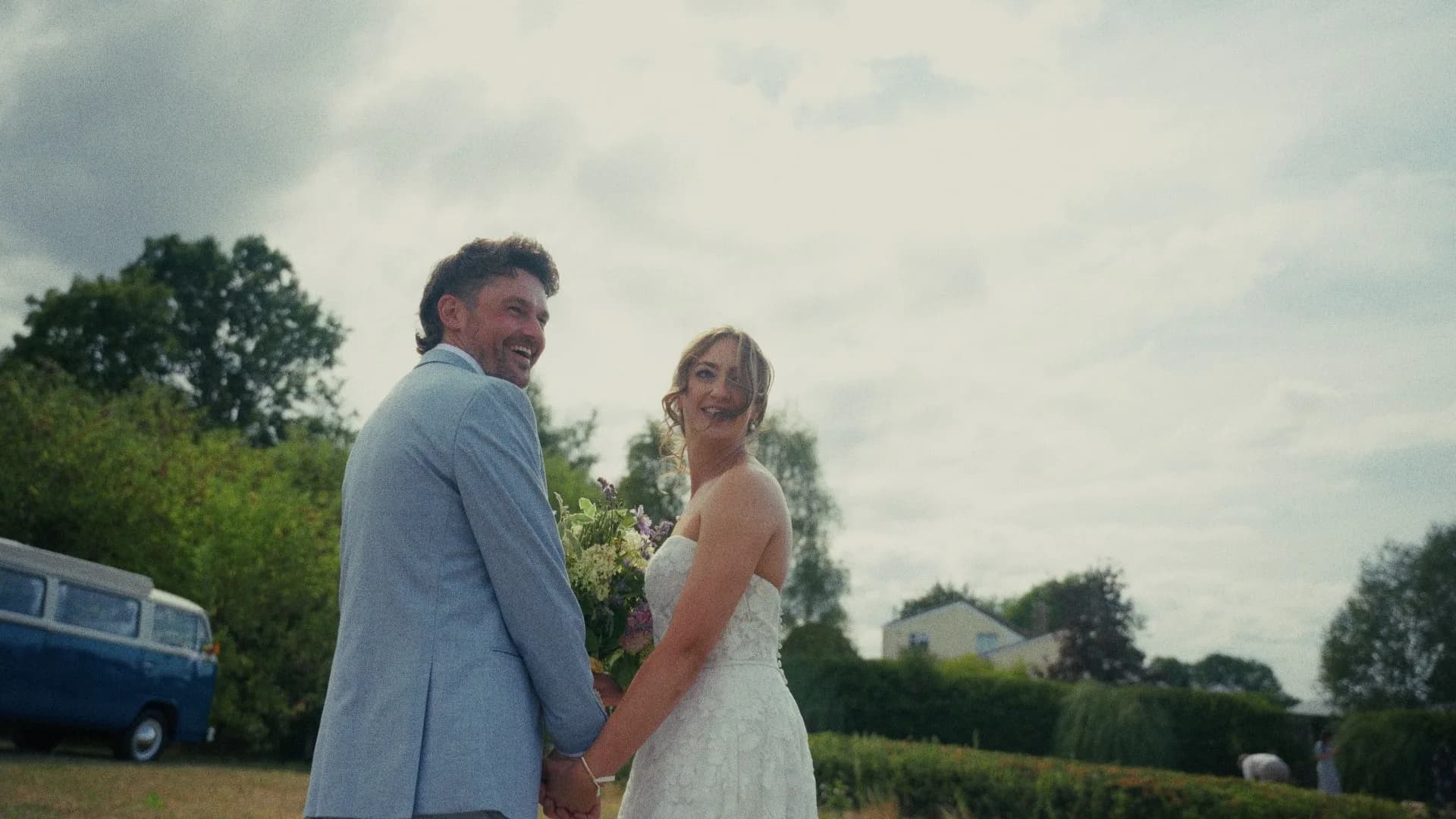 Michelle & Tim hand in hand in a garden, both looking back and laughing